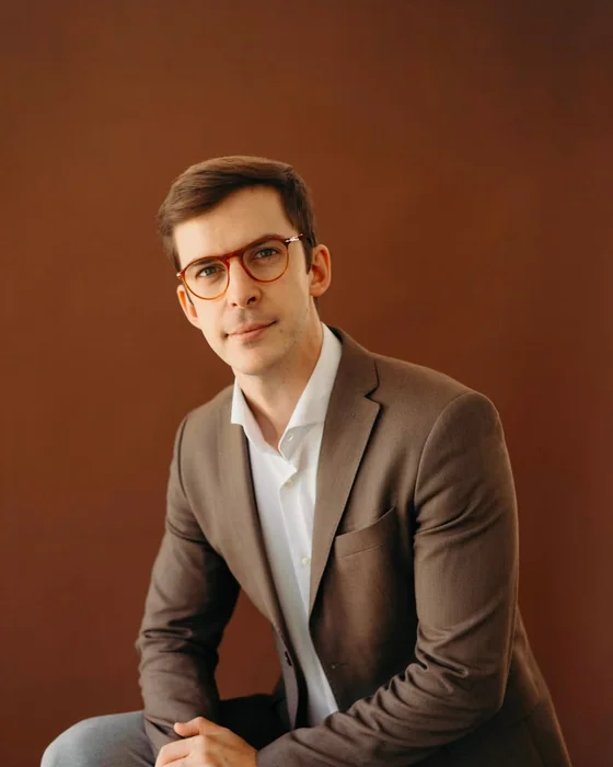 Dr. João Gubert, de óculos e blazer, sentado em estúdio